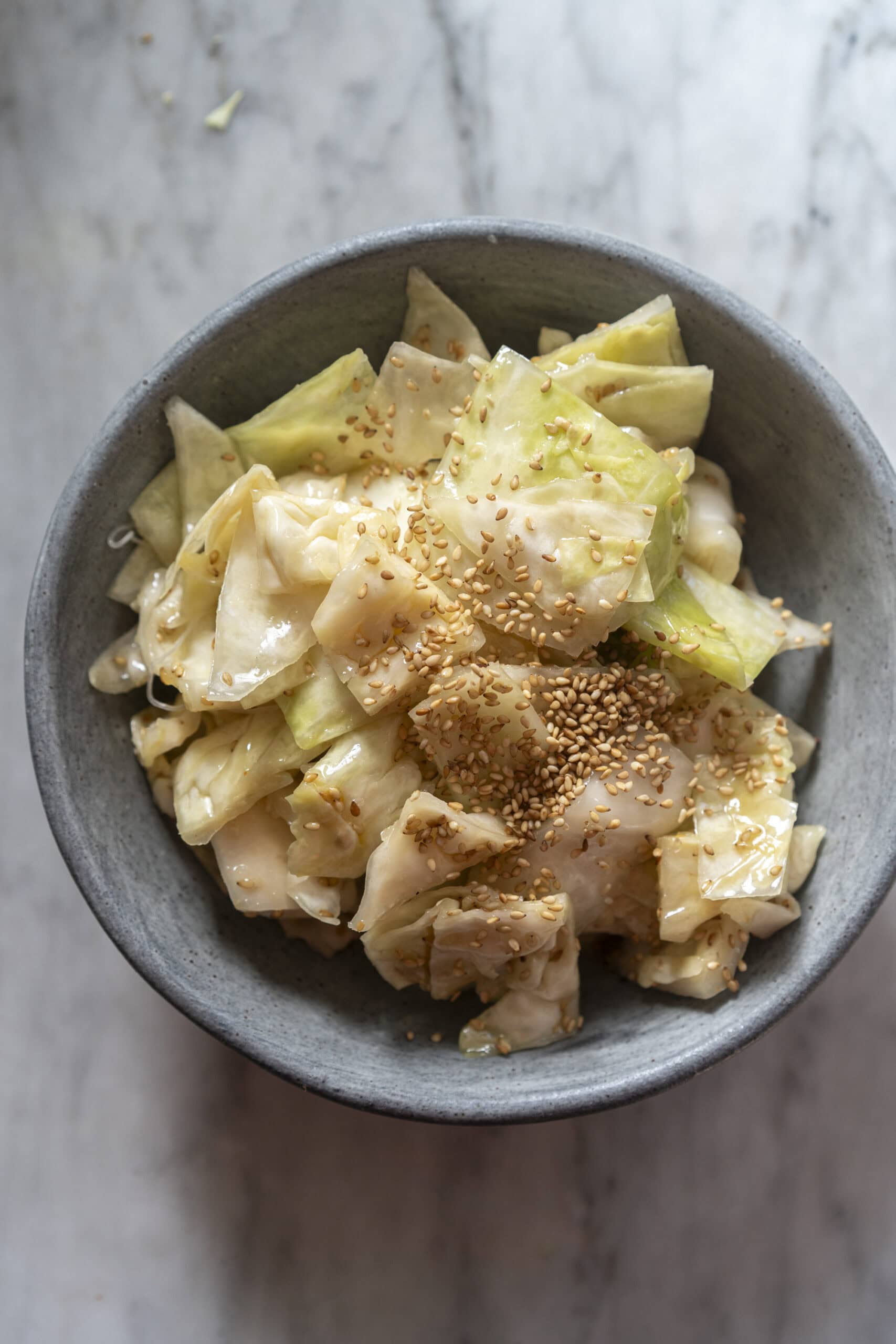 A gray bowl filled with chopped cabbage salad, dressed and topped with sesame seeds, on a marble surface.