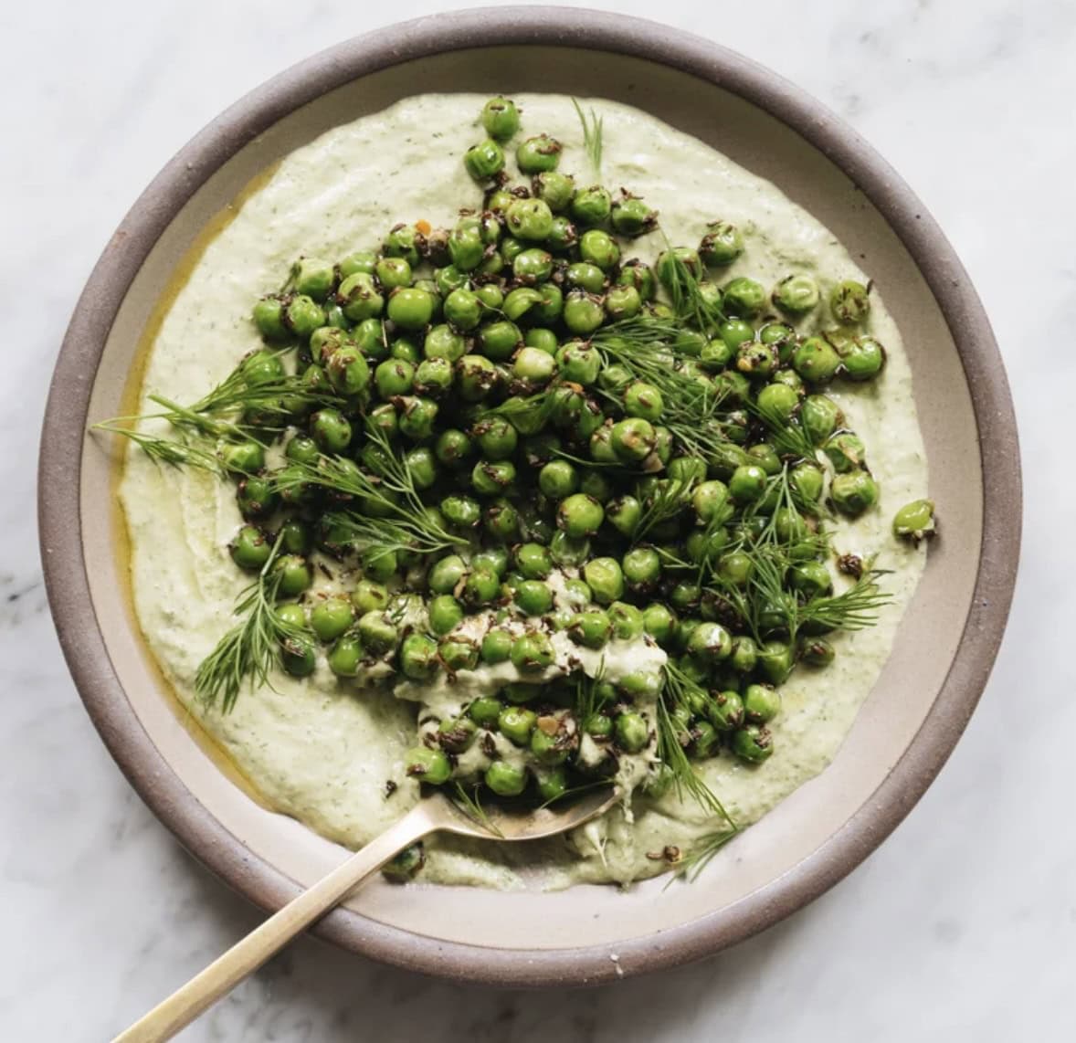 A shallow bowl with creamy green sauce topped with cooked green peas and fresh dill, with a gold spoon resting in the dish. - Hetty Lui McKinnon