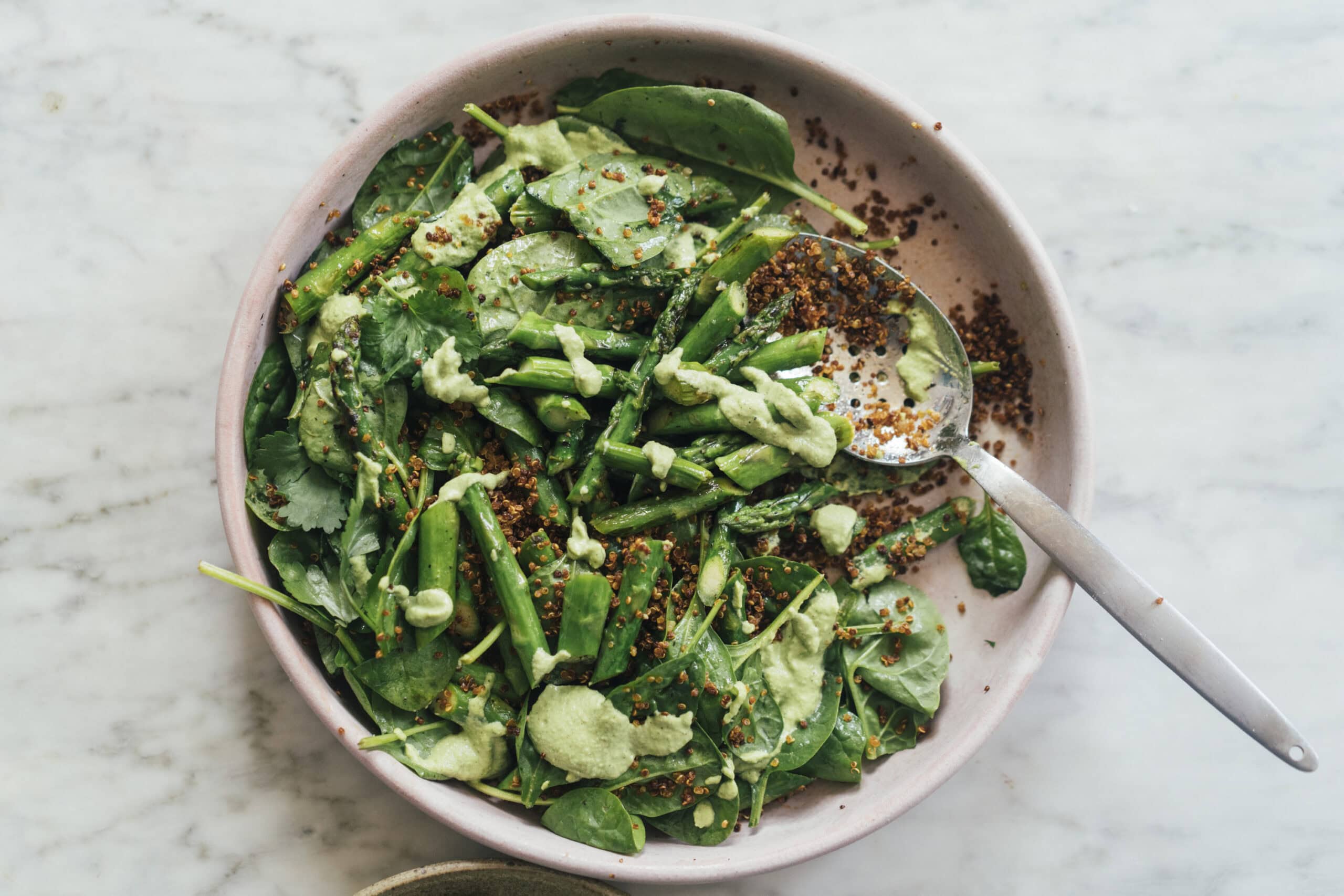 A bowl of salad with quinoa, spinach, green beans, and a creamy green dressing, with a spoon on the side.