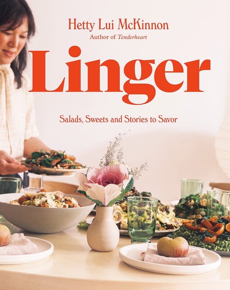 A woman sets a table with plates of salads, a flower vase, green glasses, and apples. The book title "Linger" by Hetty Lui McKinnon is prominently displayed.