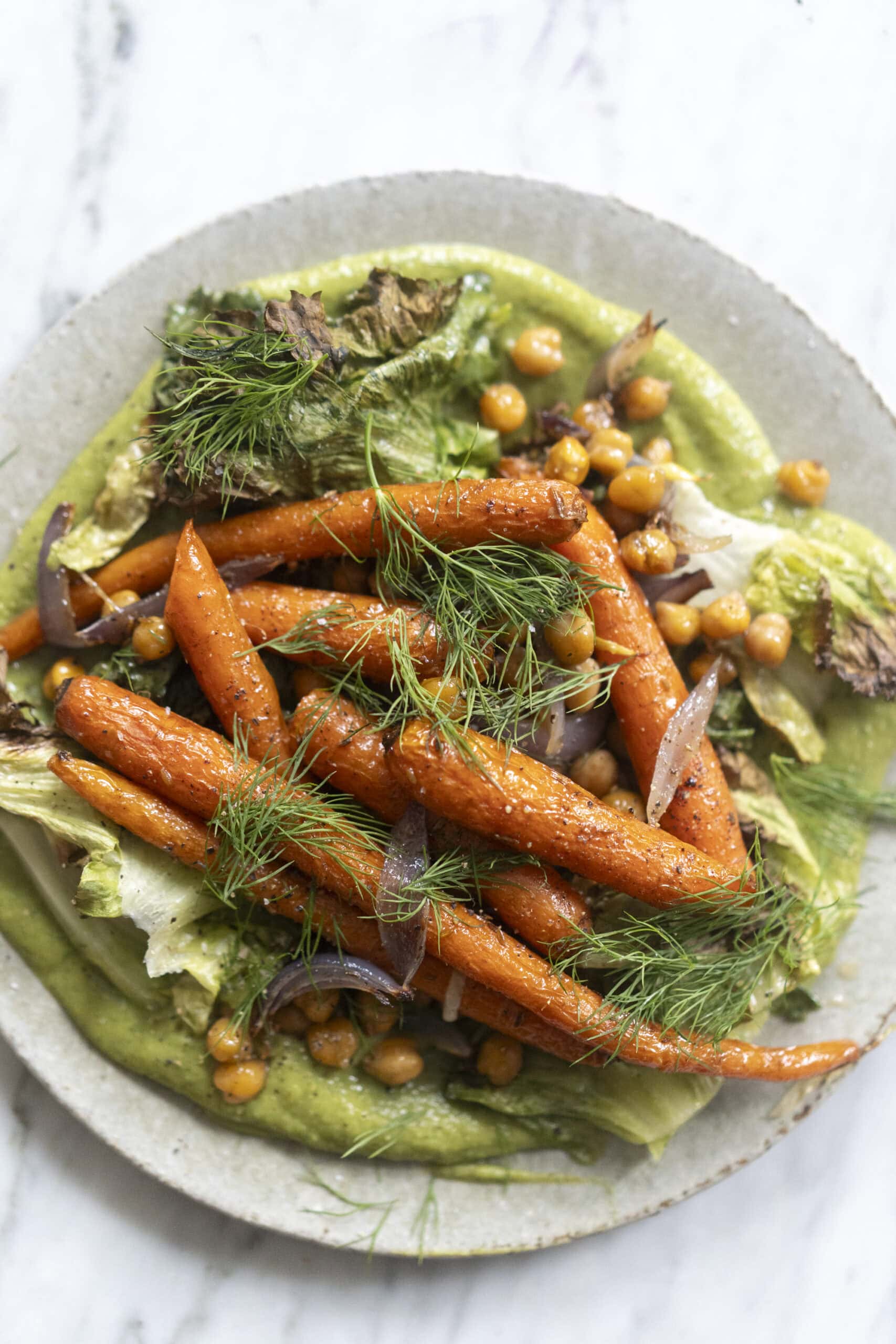 A plate of roasted carrots, chickpeas, red onion, and greens served over a green sauce, garnished with fresh dill.