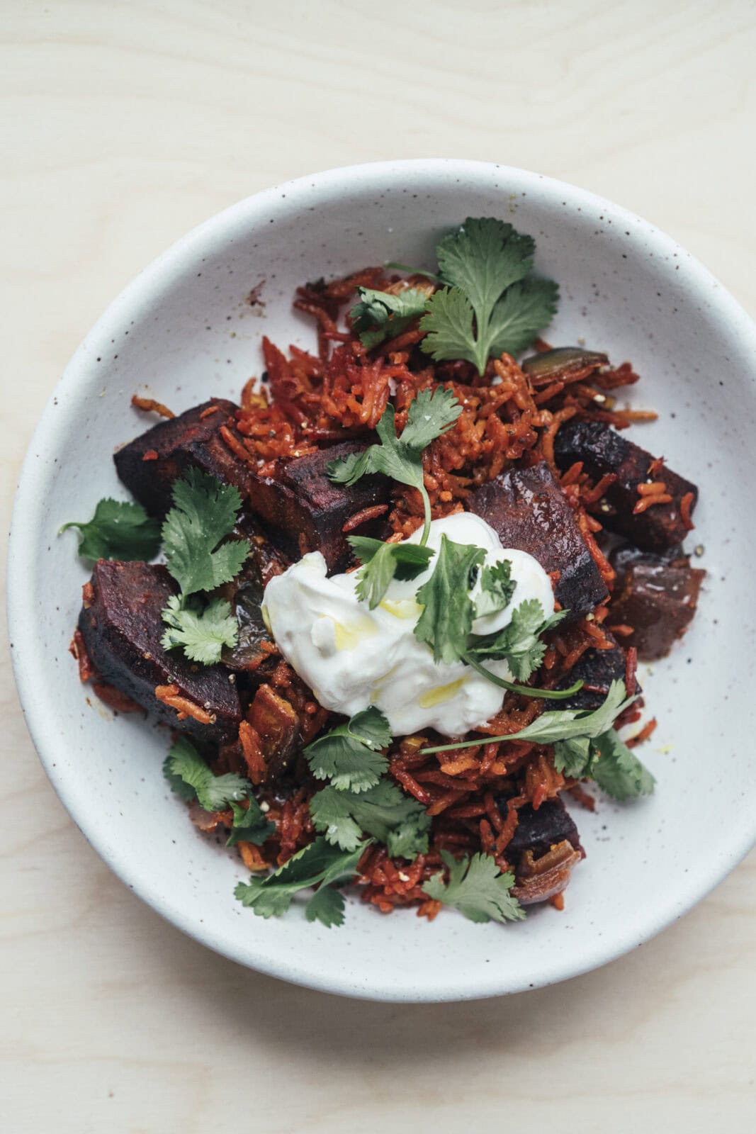 A white bowl filled with roasted vegetables and rice, topped with a dollop of sour cream and garnished with fresh cilantro.