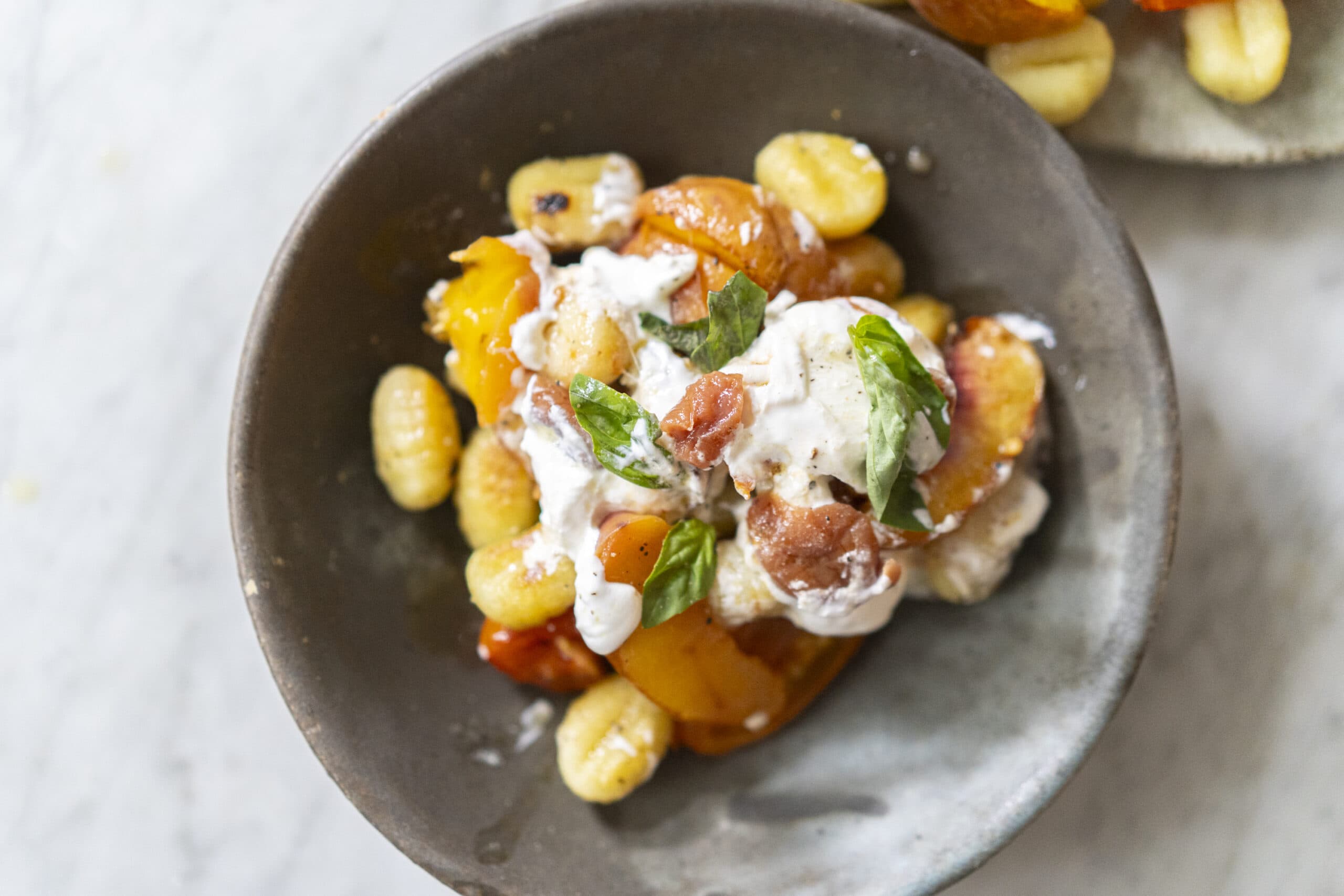 A bowl of gnocchi topped with roasted tomatoes, a dollop of ricotta cheese, and fresh basil leaves.
