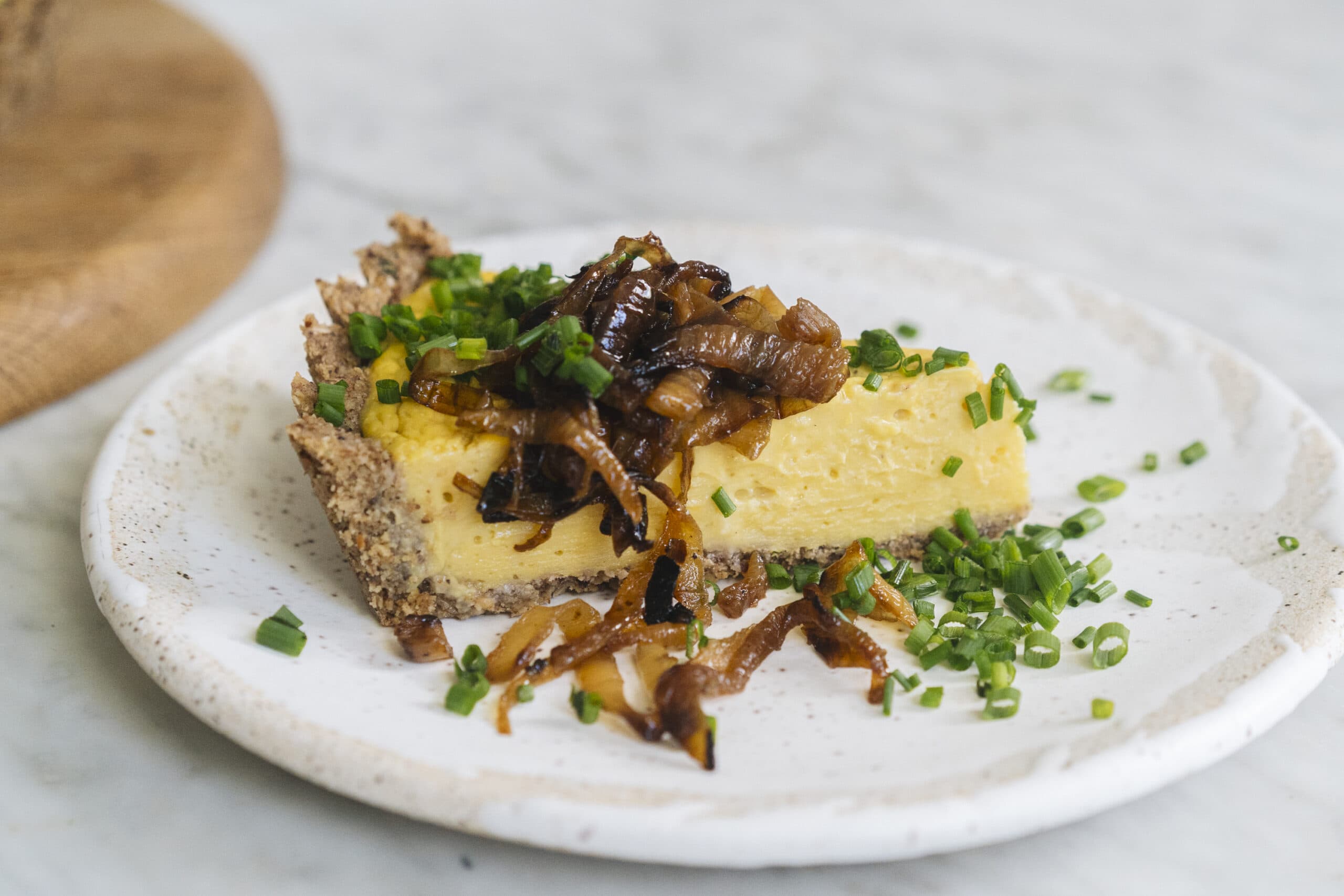 A slice of savory pie topped with caramelized onions and chopped chives, served on a white ceramic plate.
