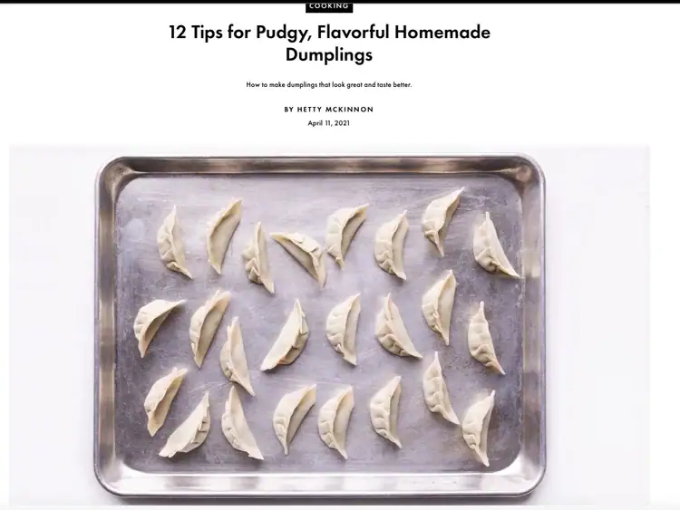 A baking tray with 24 uncooked dumplings arranged evenly in rows on a white surface.
