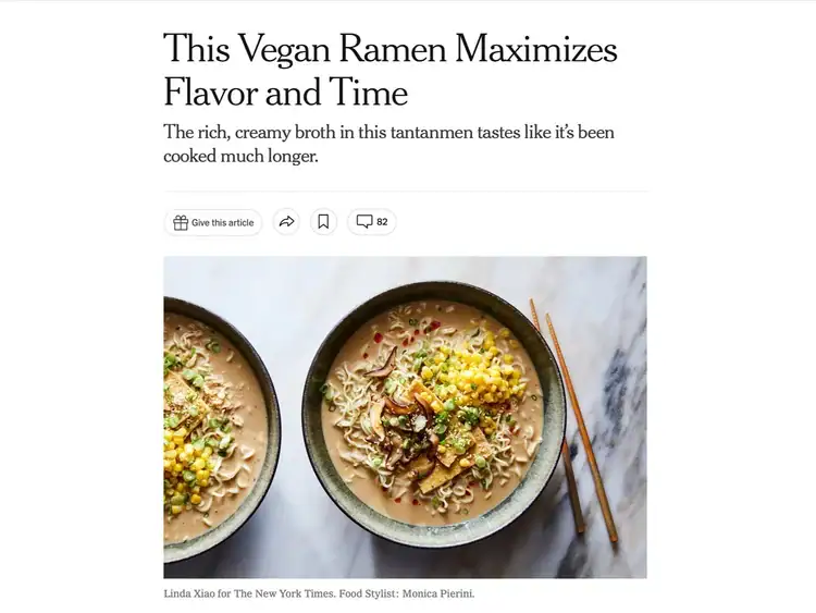 Two bowls of vegan ramen topped with corn, scallions, tofu, and sesame seeds are placed on a white surface with chopsticks resting on one bowl.