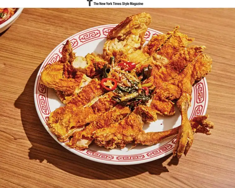 A plate of deep-fried soft-shell crab garnished with sliced red chili peppers and herbs, served on a patterned plate on a wooden table.