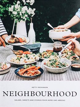 Cover of the cookbook "Neighbourhood" by Hetty McKinnon, showing hands serving salads and dishes on an outdoor table set with various plates of food.